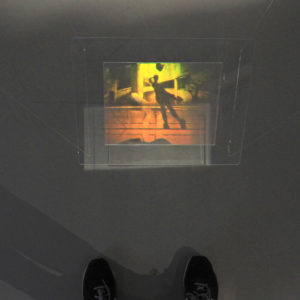 Image of art hologram Down from the Peak by Martina Mrongovius the hologram shows a shadow and reflection of the photographer and has been photographed so that you can see the photographers feet