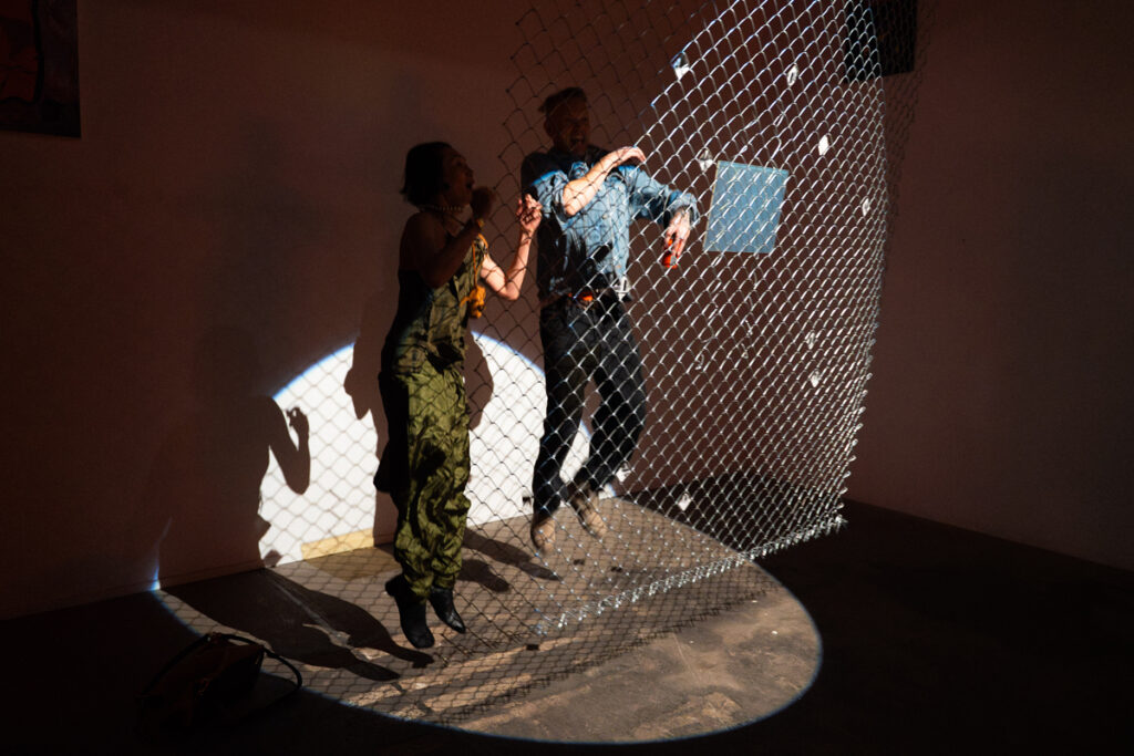 documentation of installation showing people looking at a hologram and pinhole photos in a chain link fence at the exhibition Middles. photos by Jian Peters
