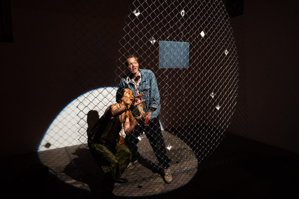 documentation of installation showing people looking at a hologram and pinhole photos in a chain link fence at the exhibition Middles. photos by Jian Peters
