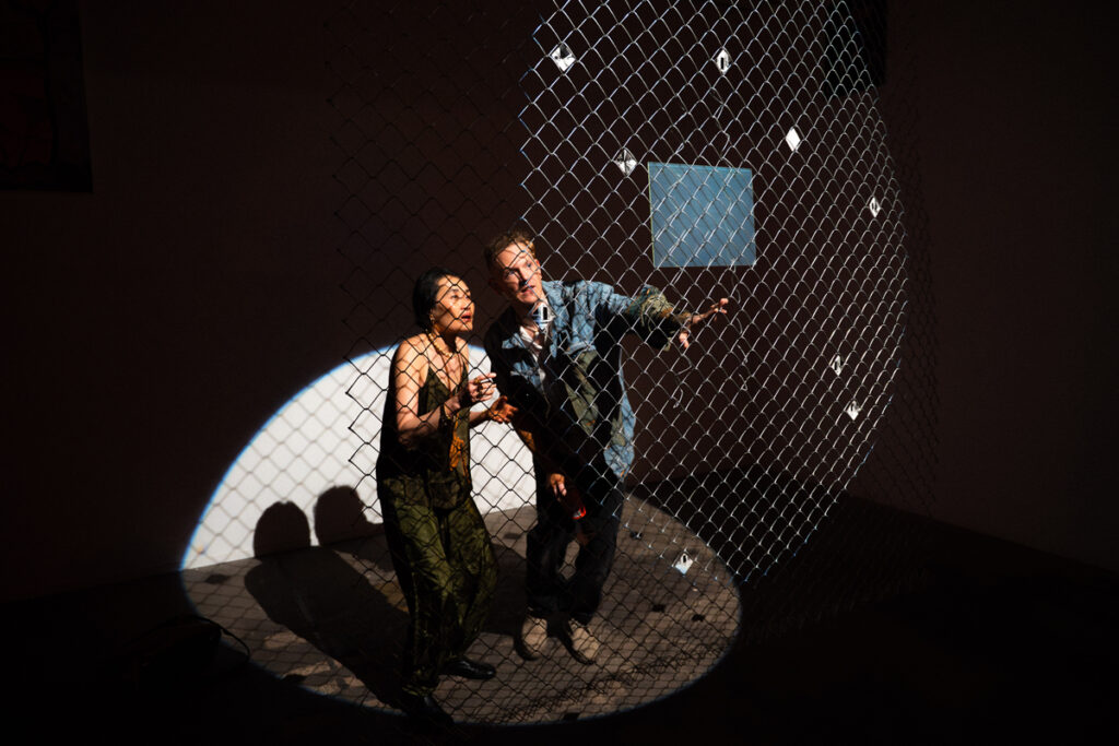 documentation of installation showing people looking at a hologram and pinhole photos in a chain link fence at the exhibition Middles. photos by Jian Peters